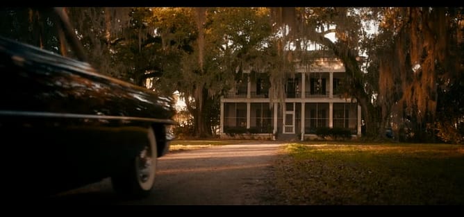 Um carro se aproximando de uma grande mansão entre árvores